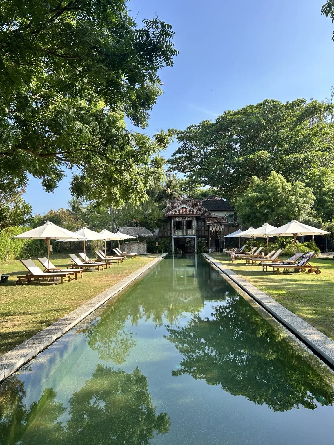 Dlouhý bazén v zahradě vedoucí k historickému domu Temple Tree Resort