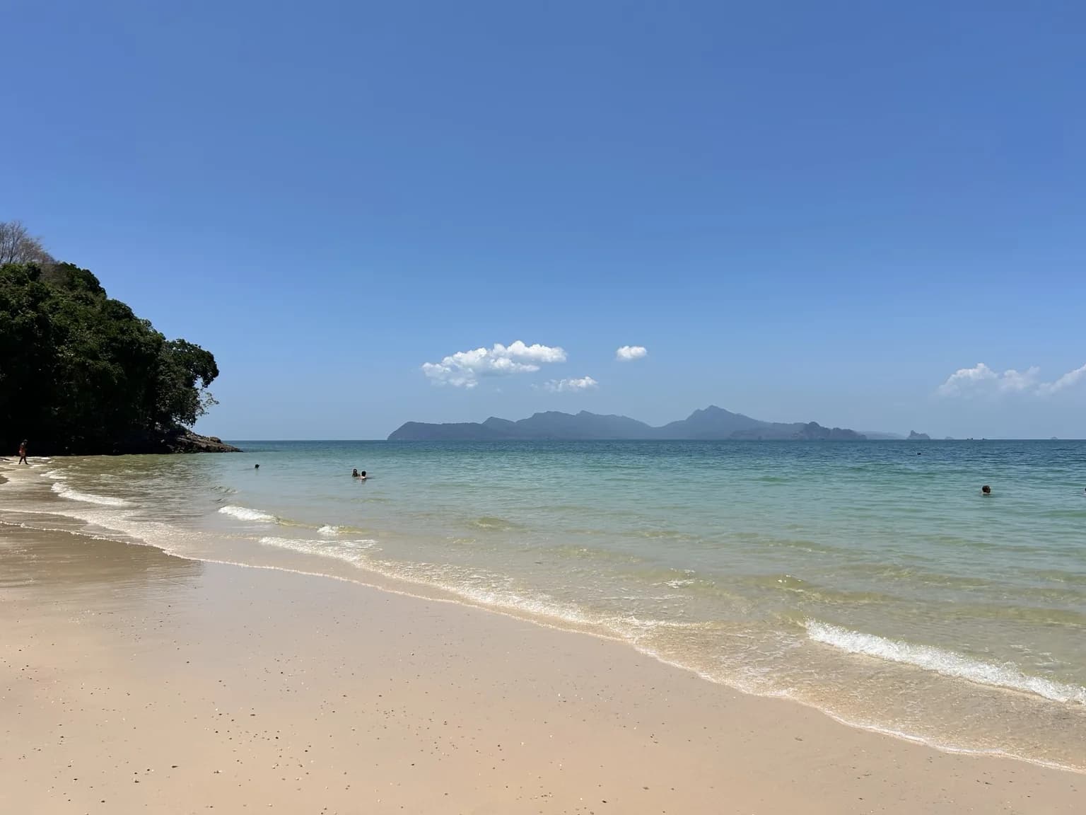 Prázdnější pláž s jemným pískem a zelenými ostrovy na obzoru na Langkawi