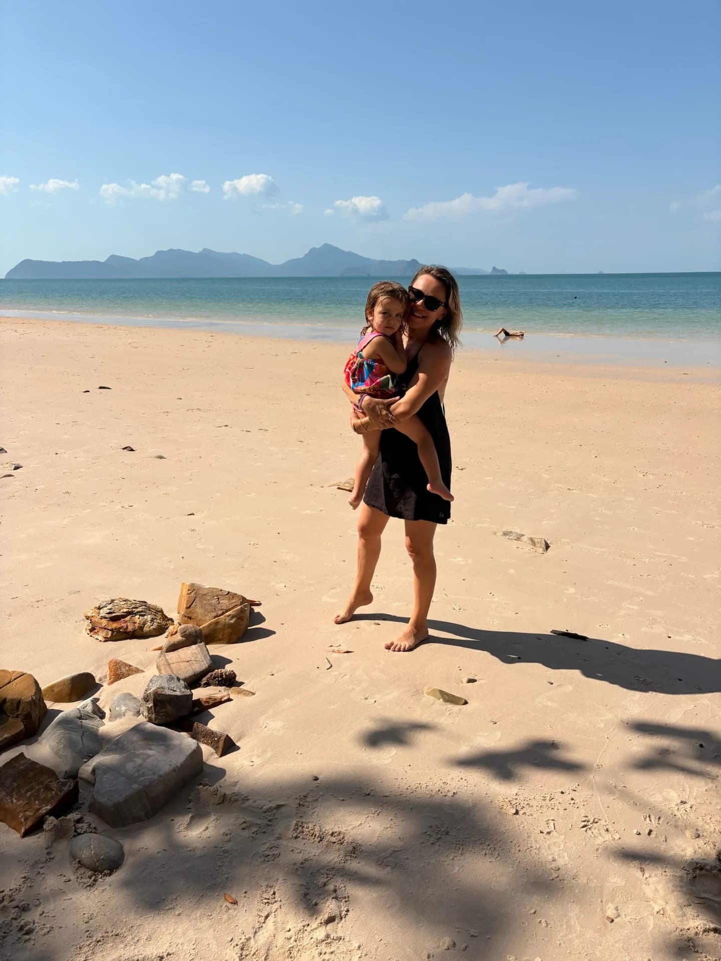 Žena s dítětem v náručí na rozlehlé pláži na Langkawi