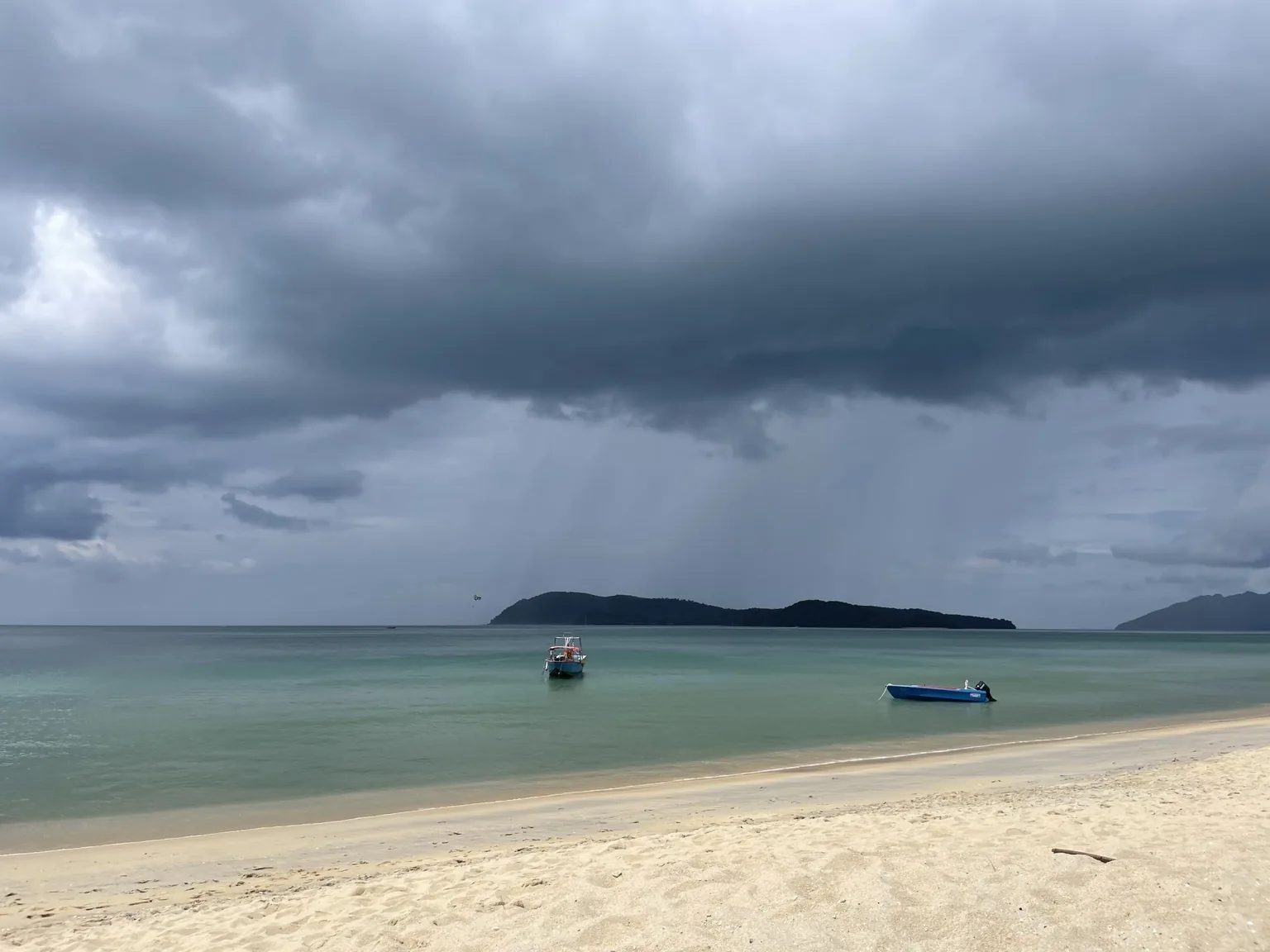Bouřkové mraky nad pláží Pantai Tengah a dvěma loděmi na tyrkysovém moři na Langkawi