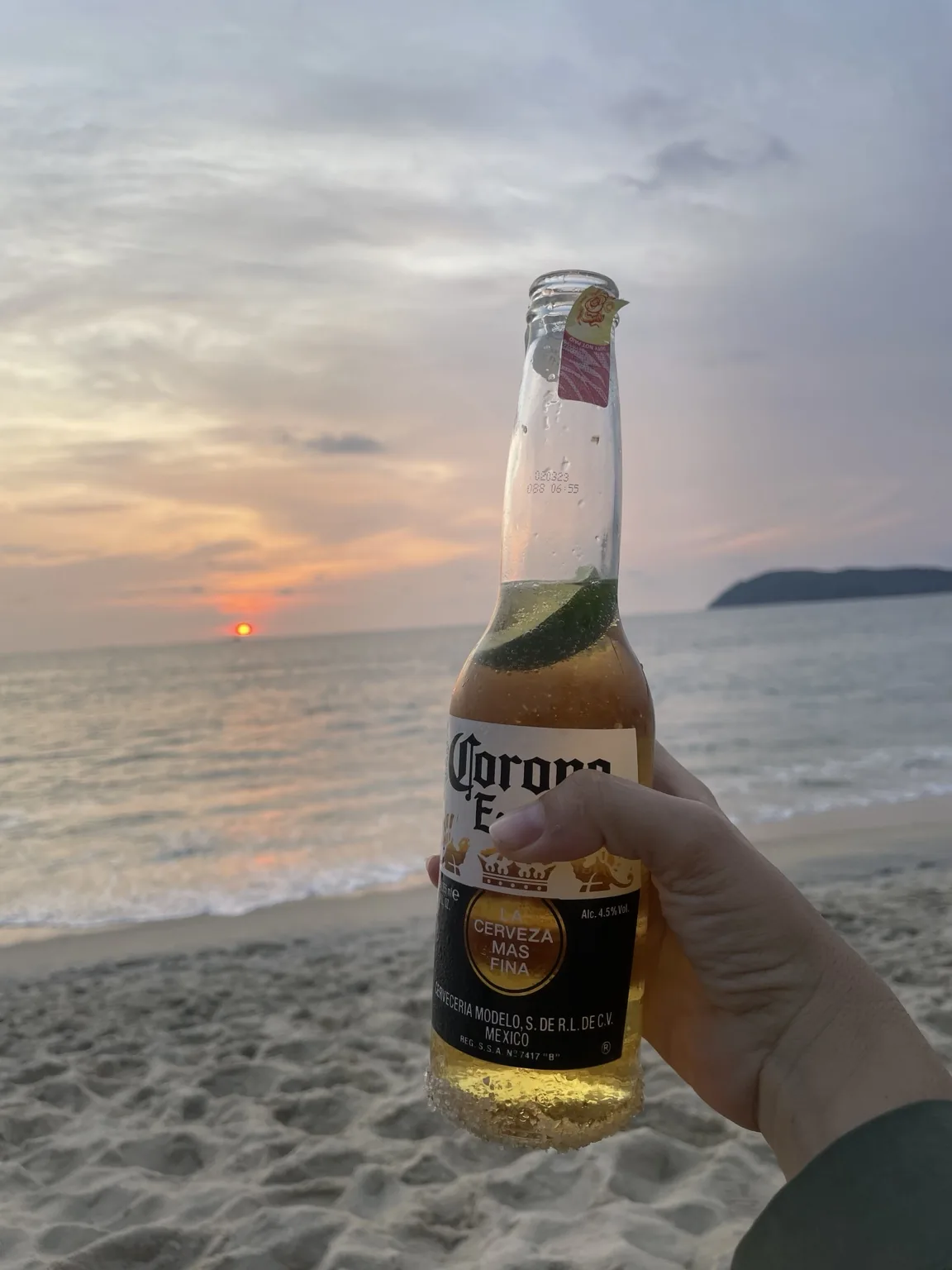 Lahev piva před mořem při oranžovém západu slunce na Langkawi