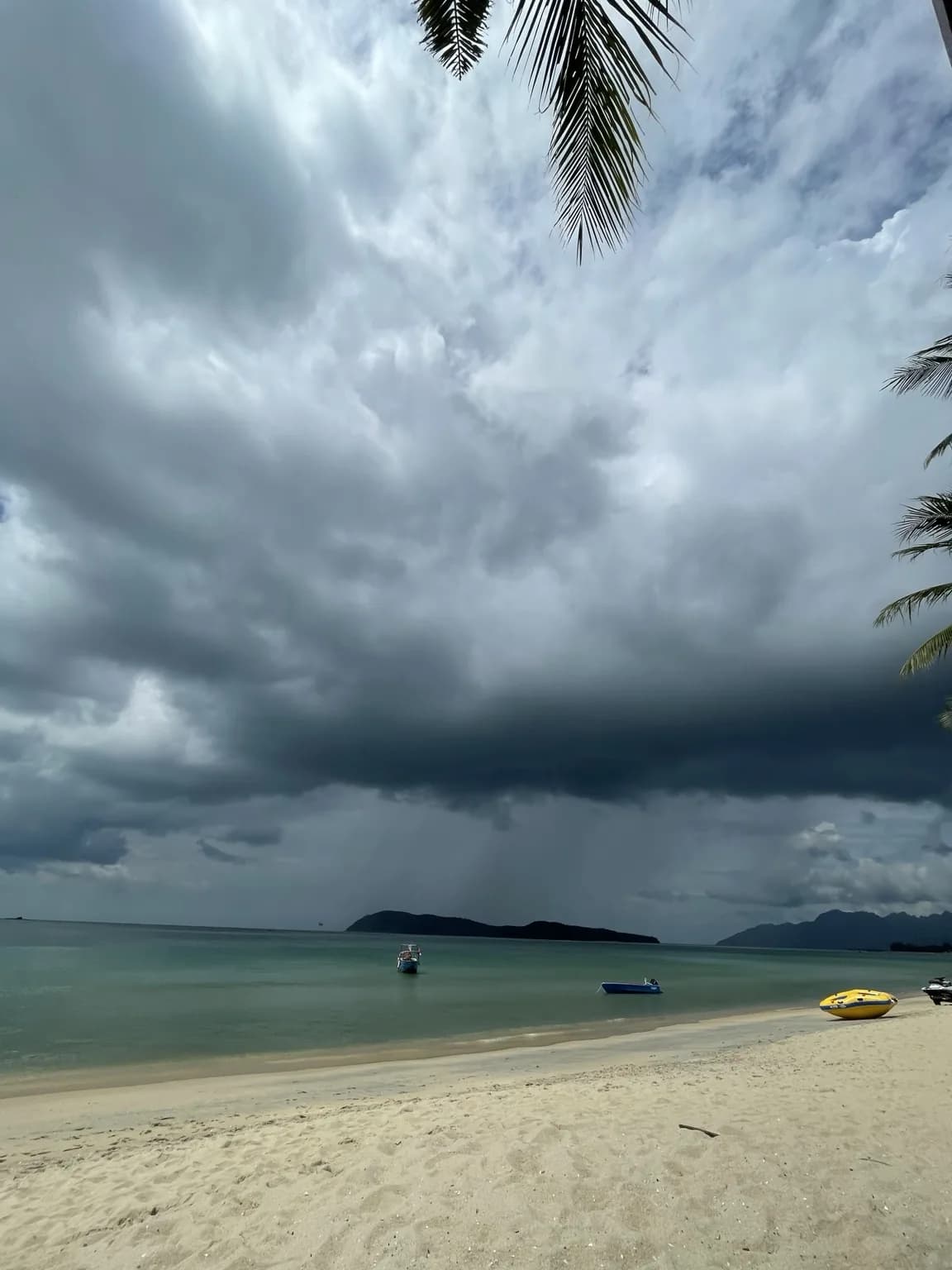 Tmavé bouřkové mraky nad tyrkysovým mořem a světlou pláží na Langkawi