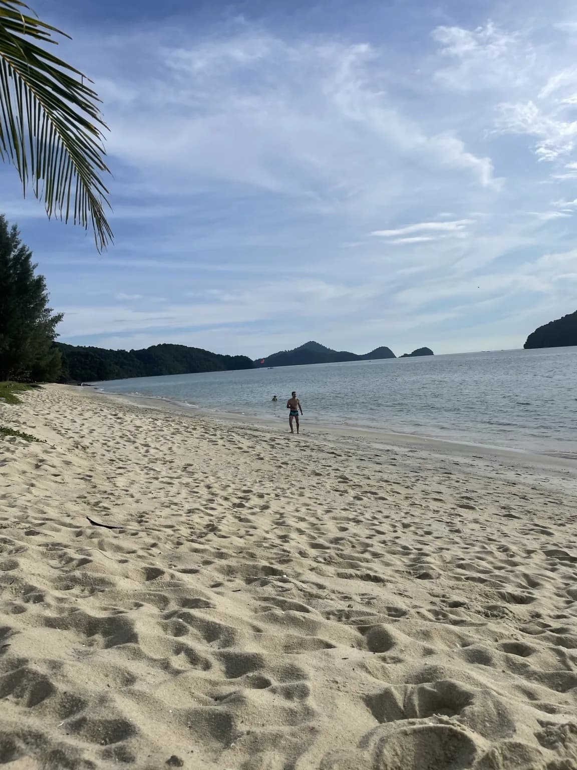 Klidná široká písečná pláž na Langkawi a ostrovy na obzoru