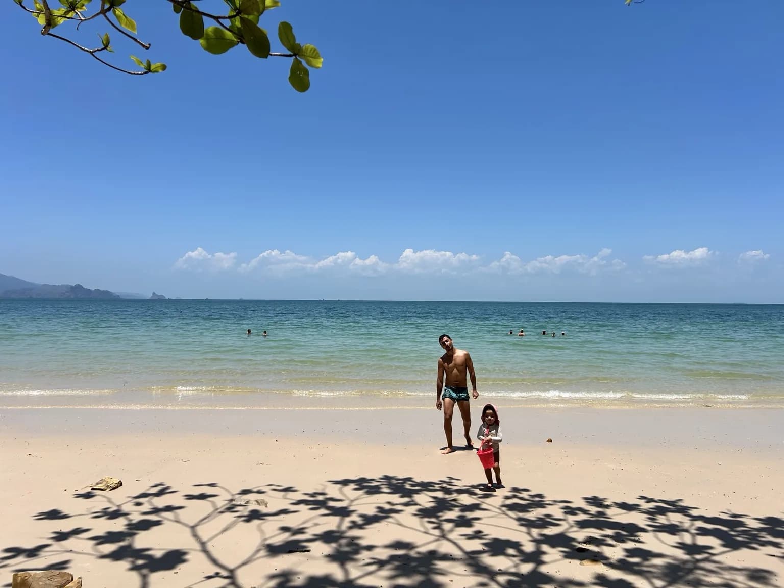 Dospělý s dítětem na světlé tropické pláži u mělkého moře na Langkawi