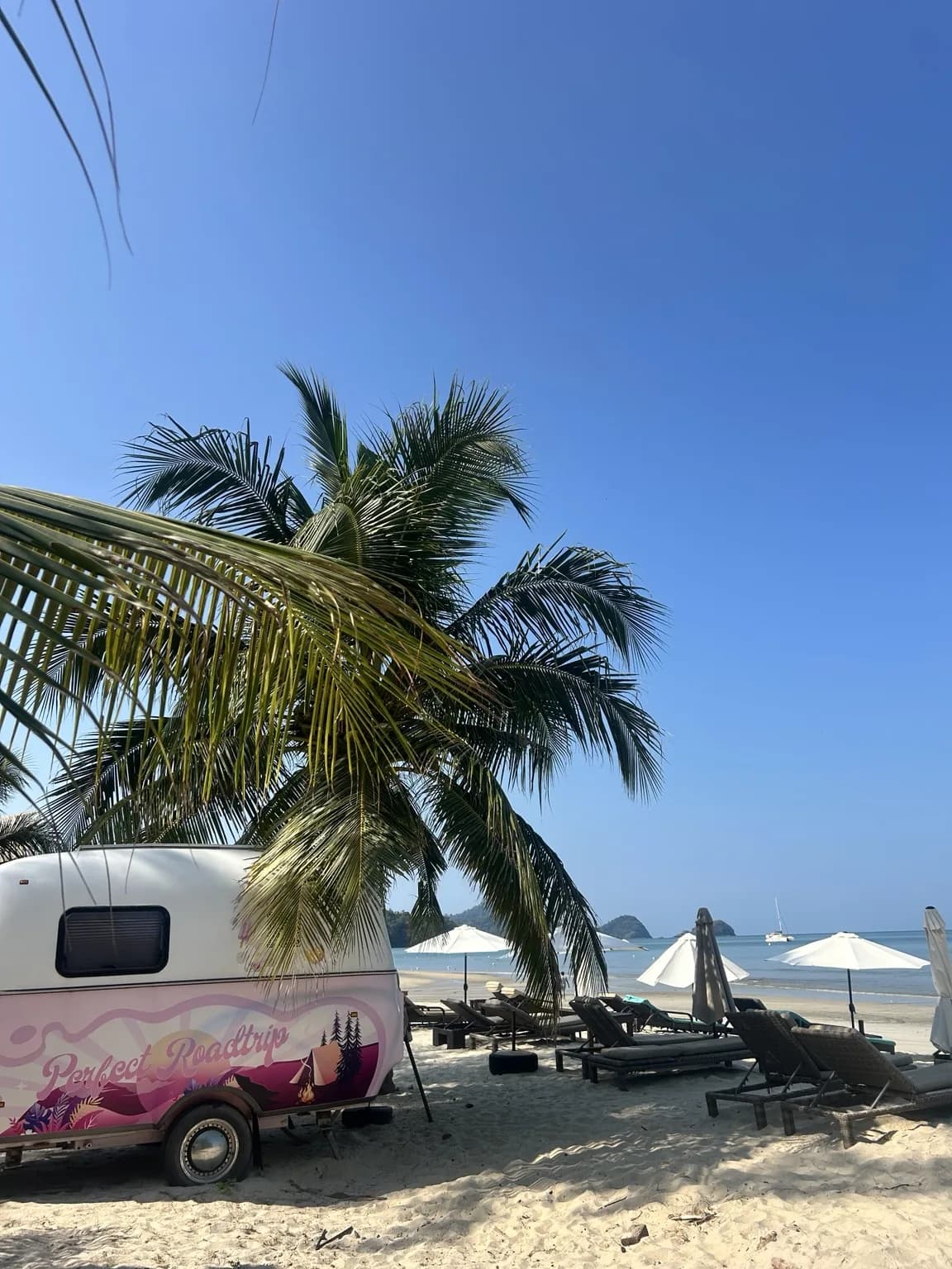 Barevný karavan pod palmami a plážová lehátka na Langkawi