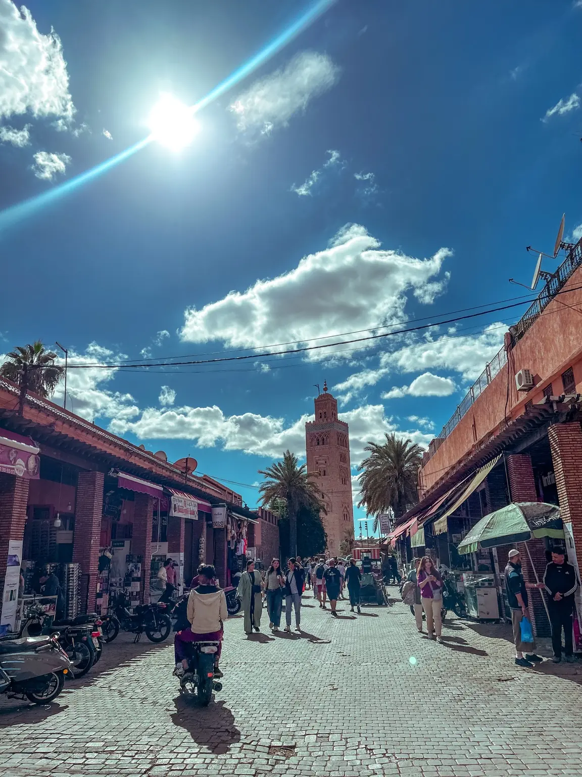 Rušná ulice Marrákeše s minaretem mešity Koutoubia v pozadí