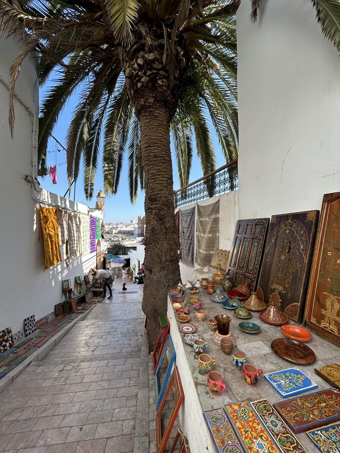 Řemeslné výrobky vystavené na schodech ve stínu palmy v Kasbah des Oudayas