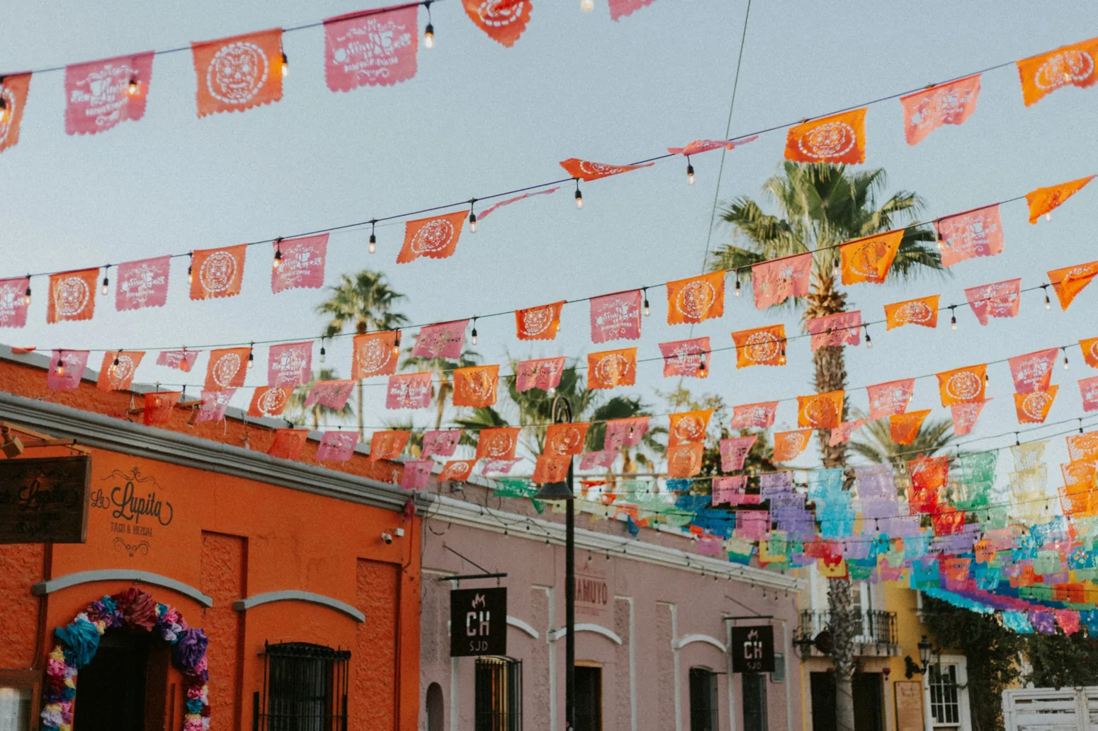 Růžové a oranžové vystřihované papírové dekorace papel picado nad mexickou ulicí