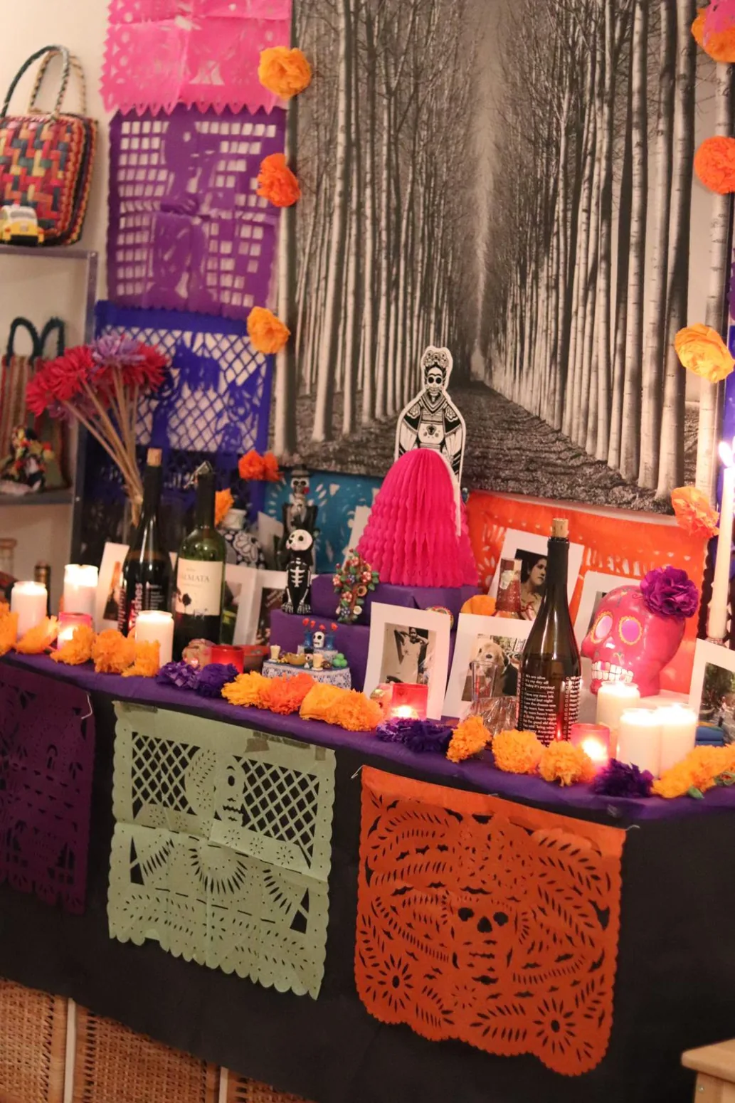 Domácí ofrenda s portréty zesnulých, svíčkami, barevnými lebkami a papel picado