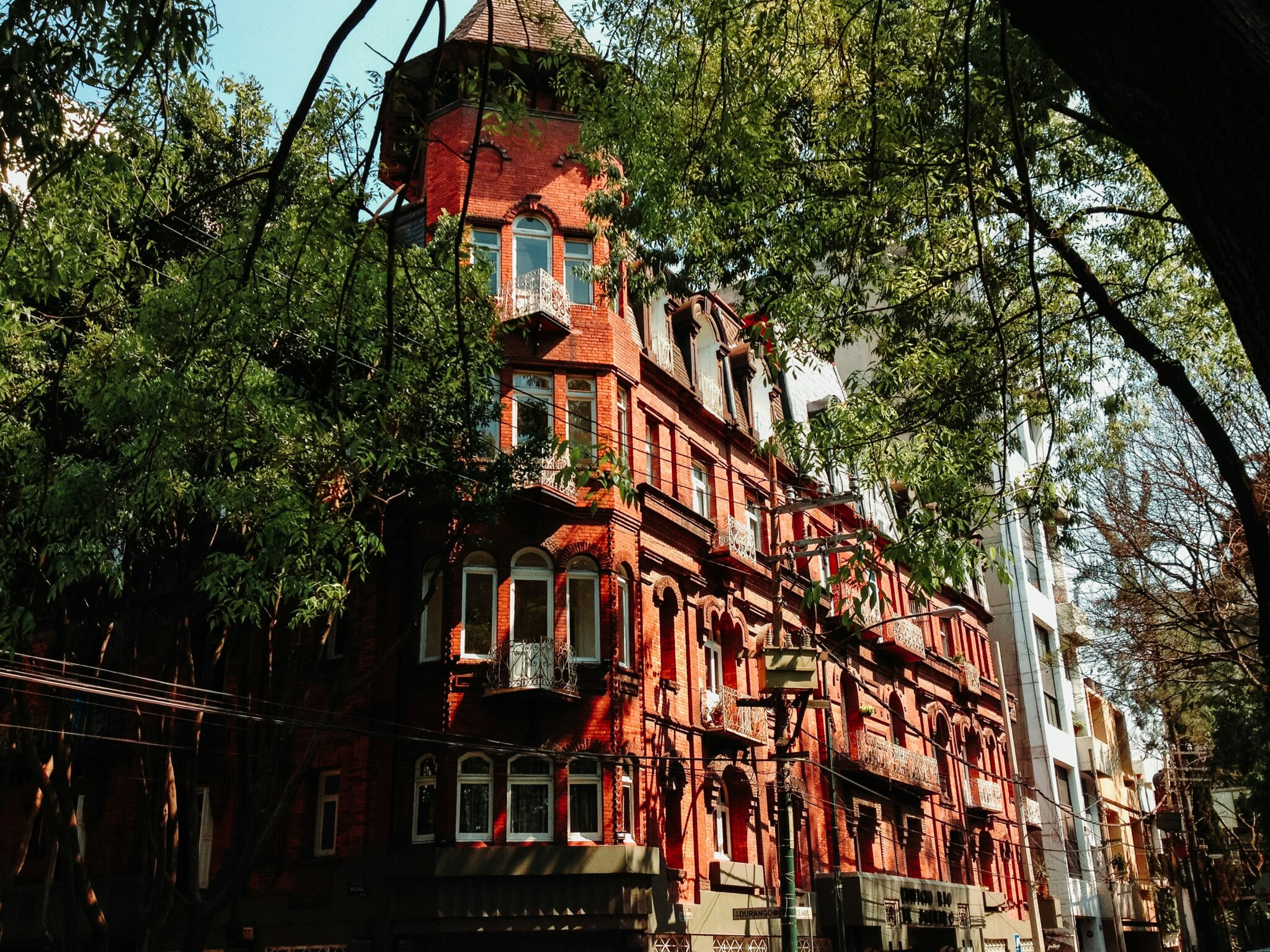 Edificio Río de Janeiro, známý jako Dům čarodějnic (Casa de las Brujas), v Colonia Roma v Mexico City, s červenou cihlovou fasádou a věžičkou obklopenou stromy.