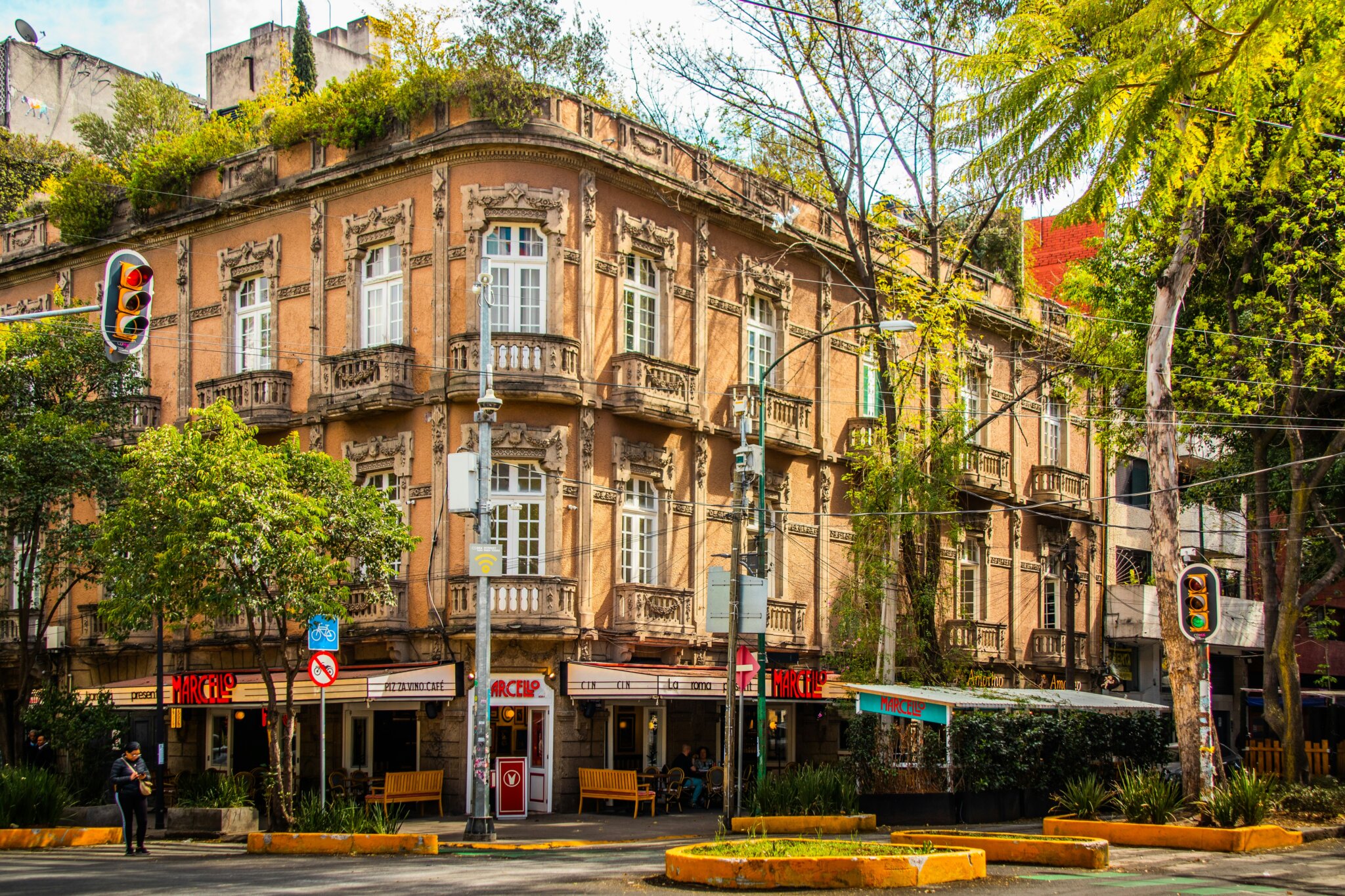Historická budova s kavárnami a restaurací Marcello v Colonia Roma, Mexico City, s typickou secesní fasádou a zelení kolem.