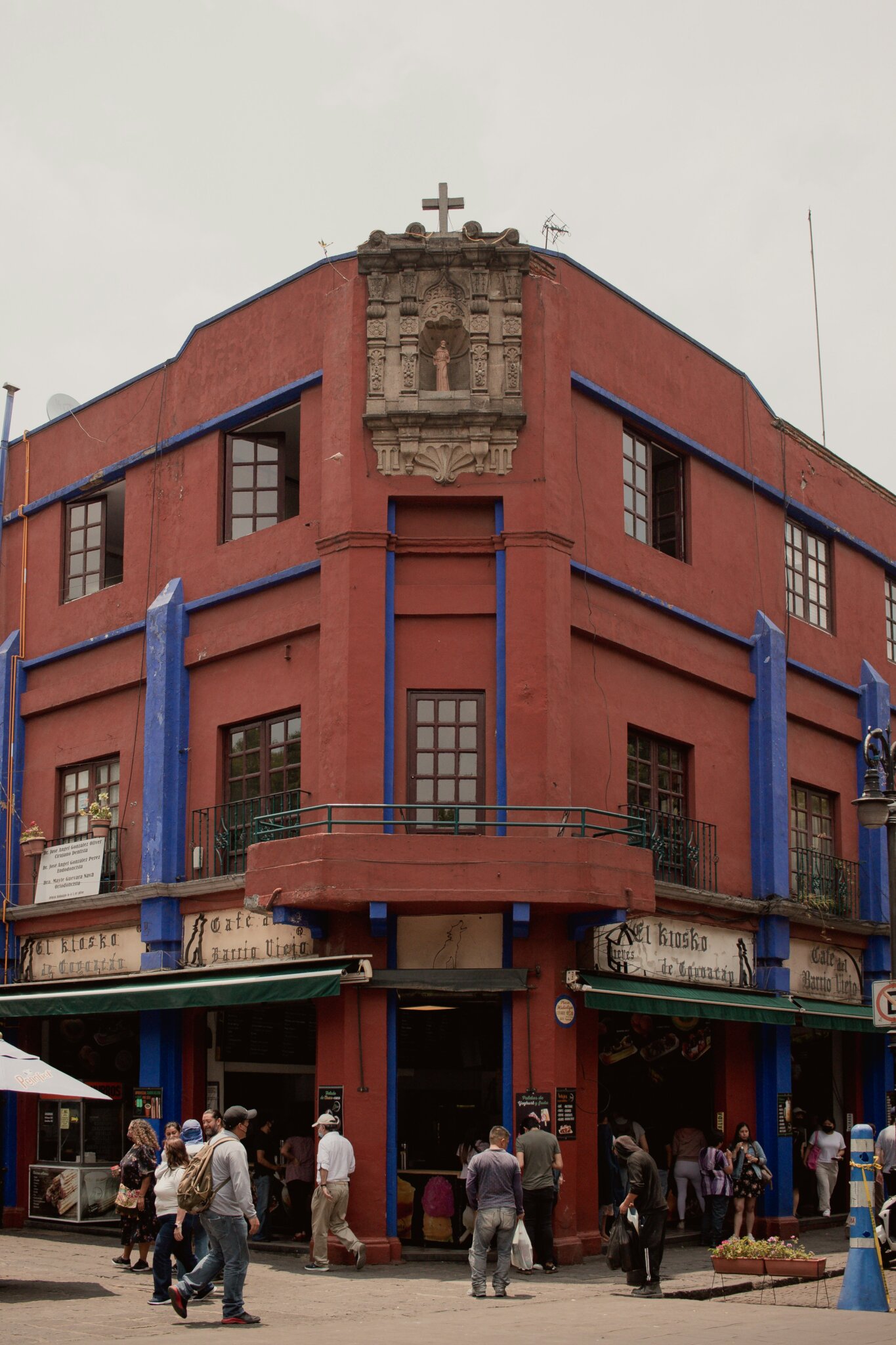 Červená a modrá historická budova v Coyoacánu v Mexico City s kavárnou El Kiosko a lidmi procházejícími ulicí - Mexico City průvodce 