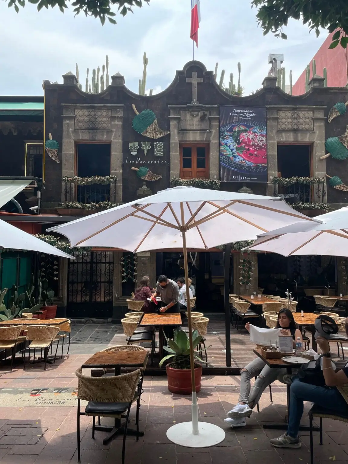 Pohled na restauraci Los Danzantes v Coyoacánu, Mexico City, s krásnou kamennou fasádou a zahrádkou se slunečníky.