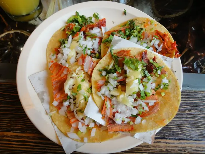 Tacos al pastor s ananasem a cibulí na bílém talíři – klasika z Mexico City.