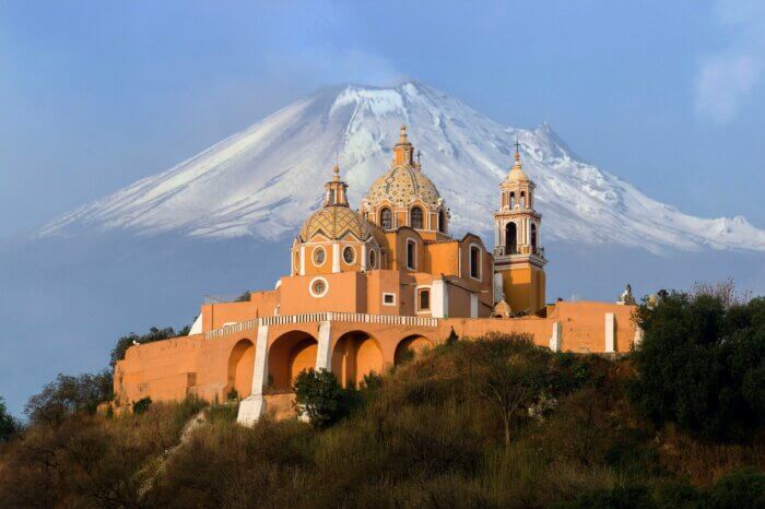 Žlutý kostel Nuestra Señora de los Remedios v Cholule s kouřící sopkou Popocatépetl v pozadí - průvodce po Mexiku