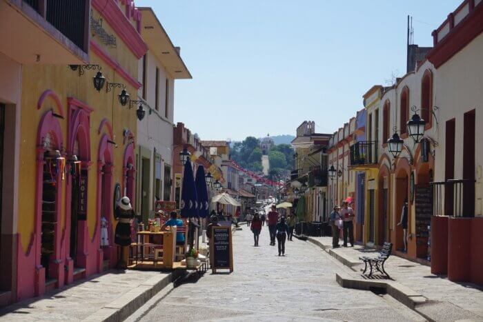 Mexiko průvodce - ulice města San Cristobal de las Casas v mexickém státě Chiapas s koloniálními domy, obchody a turisty a s kostelem na kopci v dálce